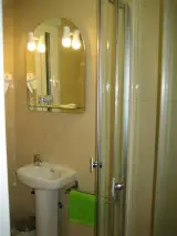 Baño con lavabo de pedestal, espejo iluminado, toalla verde y ducha con mampara de cristal